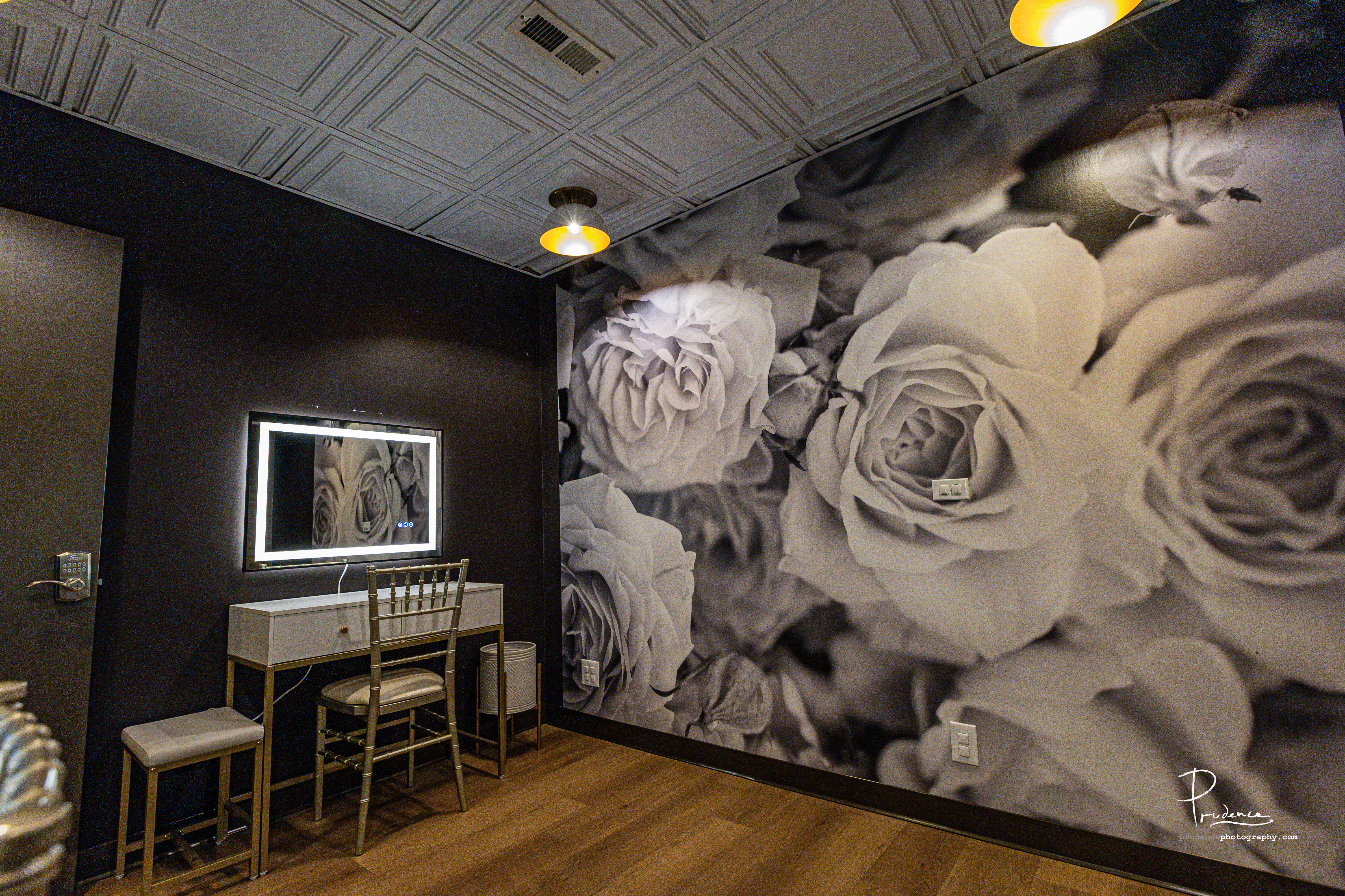 Modern vanity station with a glowing mirror, gold chair and floral mural in the prep suite