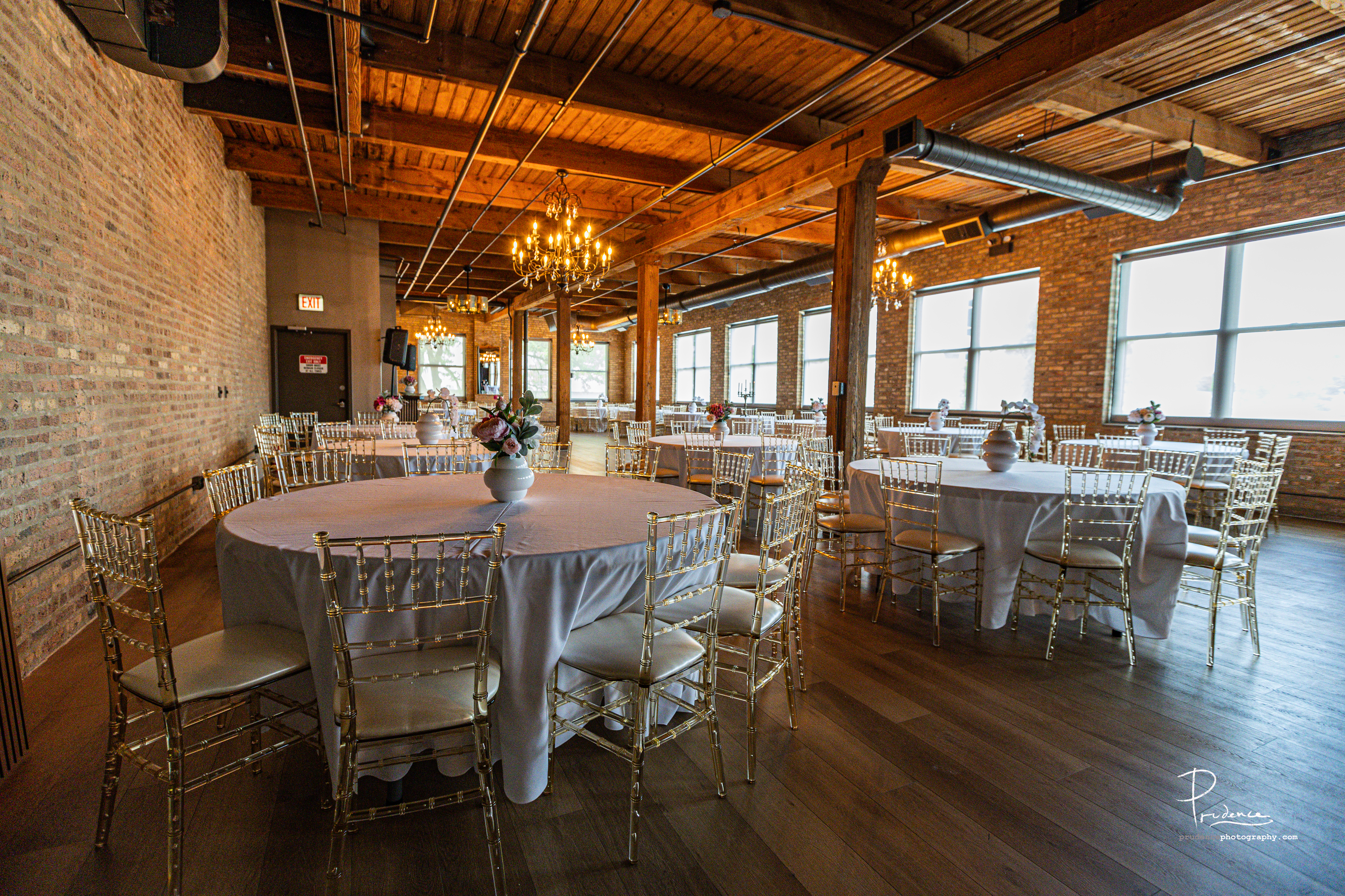 Second floor event space with exposed brick, wooden ceilings, chandeliers and banquet tables